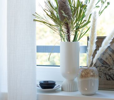 Weiße Vase auf Fensterbrett mit Prothea und Pampasgras