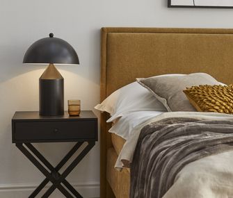 Detailbild eines Boxspringbetts in Senfgelb mit schwarzem Beistelltisch und schwarzer Lampe.