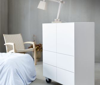 Highboard Henri auf Rollen ist wohl der schönste Stauraum - jetzt bei Homepoet online bestellen.. weißes Highhboard auf Rollen in Skandi Style Interior mit Bett und hellem Holz-Sessel mit Sitzgeflecht