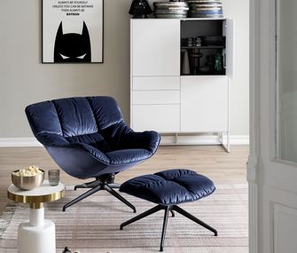 Blauer Sessel mit passendem Hocker in hellem Interior mit weißem Beistelltisch und Highboard