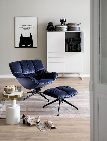 Blauer Sessel mit passendem Hocker in hellem Interior mit weißem Beistelltisch und Highboard