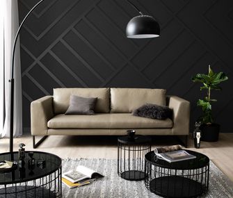 Ledersofa in der Farbe Cappuccino in modernem Wohnzimmer vor schwarzer Wand.