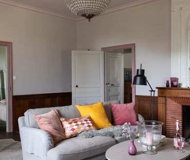 Wohnzimmer mit grauem Sofa und bunten Kissen neben Kamin.