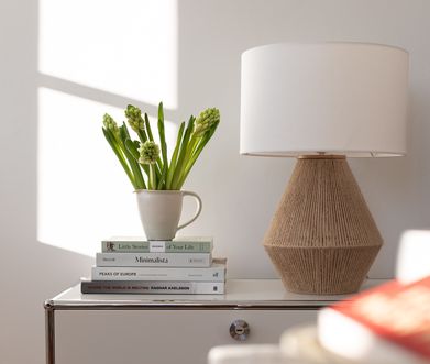 Moderne Tischleuchte auf Sideboard neben frischen Blumen.