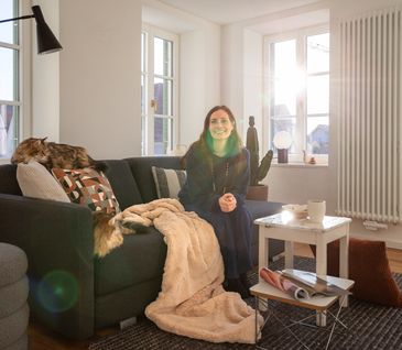 Nicole Zweig sitzt auf Sofa in gemütlichem Wohnzimmer. Dekoriert mit Kissen und Wohndecke.