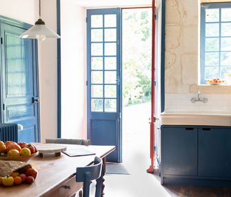 Küche im Retro-Stil mit blauen Küchenfronten, und passend gestrichener Tür und Esszimmerstühlen an Holztisch.