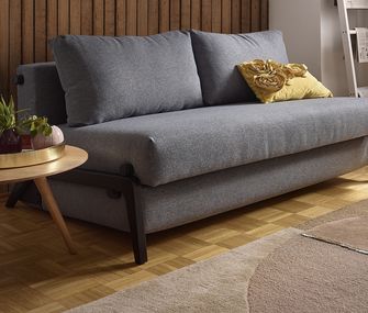 Graues Funktionssofa mit einem gelben Deko-Kissen neben einem dekorierten Couchtisch