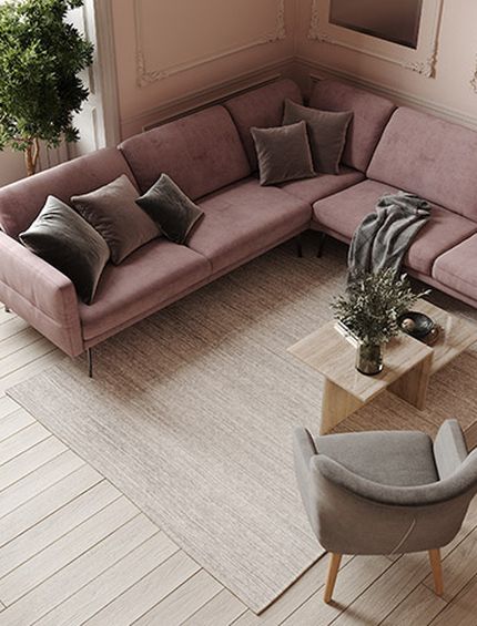 Sicht von oben auf Ecksofa aus altrosa Stoff mit kleinem Beistelltisch aus Holz und beigem Sessel auf hellem Teppich.