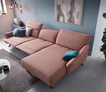 Rosa Stoffsofa mit Relaxfunktion vor hellblauer Wand mit blauen Kissen dekoriert.