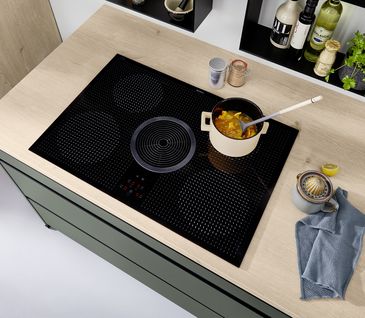 Nahaufnahme eines modernen Kochfelds mit Muldenlüfter in Arbeitsplatte mit heller Holzoptik.