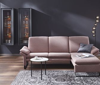 Rosa Ecksofa in einem modernen Wohnzimmer mit kleinem Beistelltisch vor dunkler Wand.