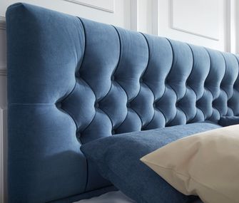 Detailansicht von Bett-Rückenlehne mit blauem Stoffüberzug und Zierknöpfen
