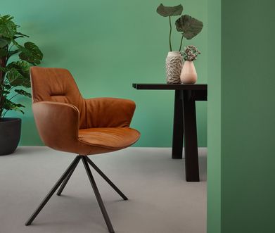 Esszimmerstuhl mit Leder in der Farbe Cognac vor grüner Wand.