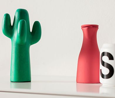 Ein grüner Deko-Kaktus mit einer roten Vase und einer Tasse mit aufgedrucktem „S“