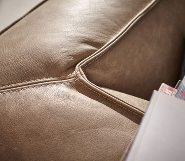 Detailansicht von hellbraunem Ledersofa mit hellgrauem Kissen dekoriert