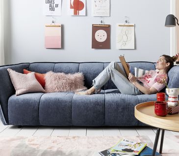 Blaues Sofa mit passendem Hocker in jung eingerichtetem Wohnzimmer