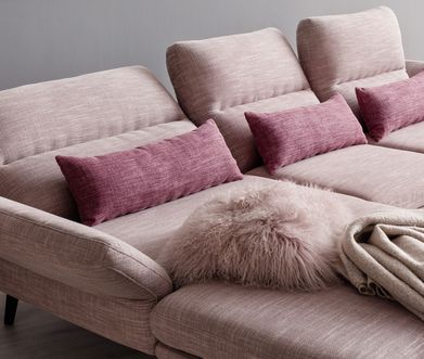 Rosafarbiges Funktionssofa mit Longchair und rosafarbigen Kissen sowie einer Wohndecke