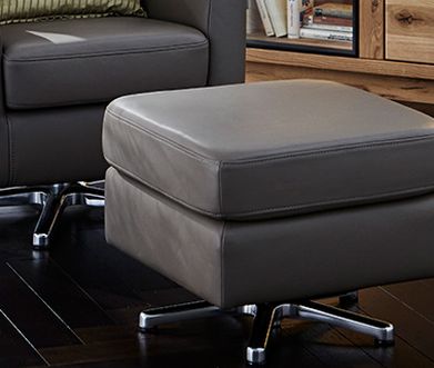 Ein Hocker kombiniert mit einem Ledersessel eignet sich perfekt zum Entspannen Viereckiger grauer Hocker aus Leder passend zu dem Sessel mit Relaxfunktion im Hintergrund