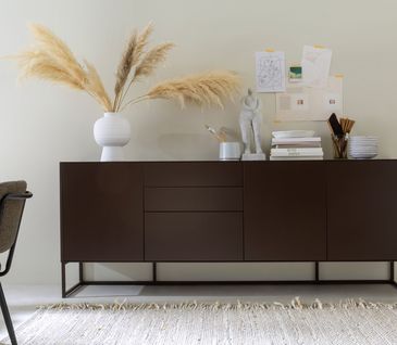 Sideboard in der Farbe Schoko-Braun vor beigem Teppich - modern dekoriert.