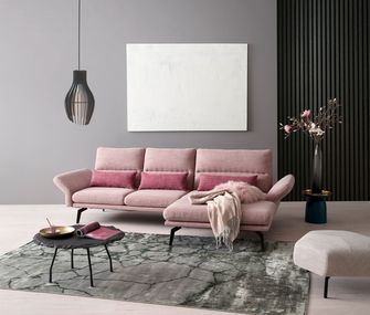 Rosa Ecksofa und weißer Hocker in großem Wohnzimmer mit schwarzem Couchtisch und grauem Teppich.