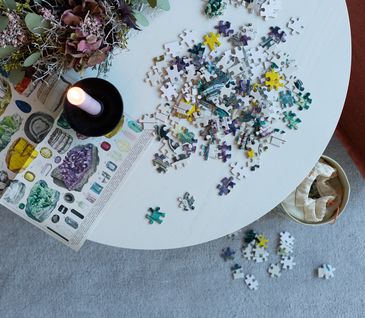 Bunte Puzzle-Teile, Kerze und Blumenkranz auf einem weißen runden Tisch