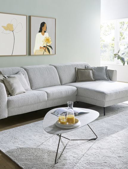 Hellgraues Ecksofa in einem hellen Wohnzimmer mit passendem Couchtisch und großem Teppich.