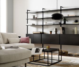 Bücherregale gibt es in verschiedenen Größen und passend für jeden Wohnstil Schwarzes Regal mit Dekoration neben einem hellen Sofa und vor einer weißen Wand