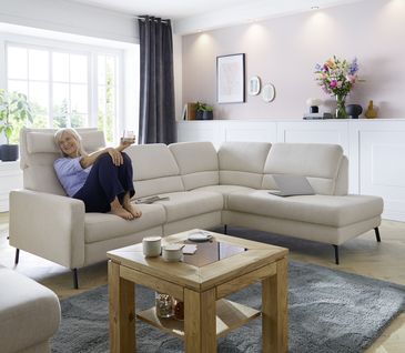 Ecksofa in beigem Stoff in hellem Wohnzimmer mit Couchtisch aus Holz.