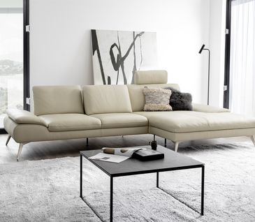 Elegantes Wohnzimmer in hellen Farben mit beigem Leder-Ecksofa und schwarzem Couchtisch.