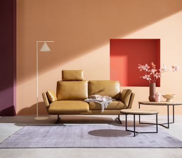 Sofa in der Farbe Cognac in modernem Wohnzimmer vor Wand in Farbe Peach mit runden Beistelltischen.