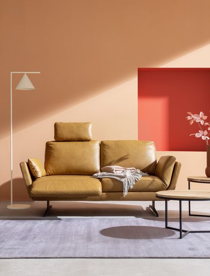 Sofa in der Farbe Cognac in modernem Wohnzimmer vor Wand in Farbe Peach mit runden Beistelltischen.