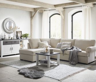 Beiges Ecksofa in hellem Wohnzimmer mit Teppich, Couchtisch und weißem Sidebaord.