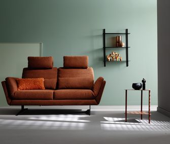 Erste Wohnung und erstes Wohnzimmer: Das Sofa ist ein Must-have! 2-Sitzer Sofa in der Farbe Rost vor grüner Wand mit Beistelltisch in minimalistischem Wohnzimmer.