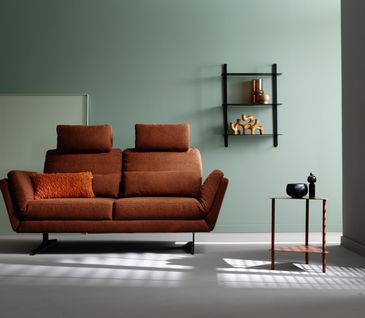 2-Sitzer Sofa in der Farbe Rost vor grüner Wand mit Beistelltisch in minimalistischem Wohnzimmer.
