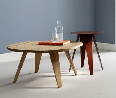 Couchtisch in Holz und Beistelltisch aus Metall in Rot auf weißem Boden vor Pastellblauer Wand.