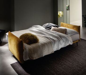 Ausgeklapptes Schlafsofa in senfgelbem Samtstoff.