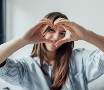 Junge Frau formt mit ihren Händen vor ihrem Gesicht ein Herz.