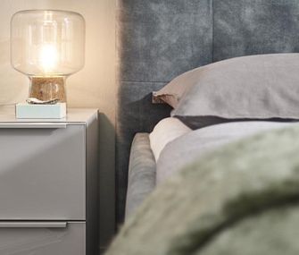 Blaugraues Boxspringbett neben Nachtkonsole in Cremetönen mit minimalistischer Tischleuchte