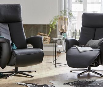 Zwei schwarze Fernsehsessel auf Leder mit einer Relaxfunktion neben einem Beistelltisch