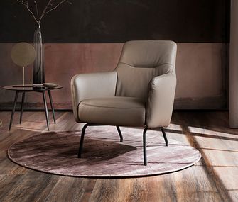Beiger Ledersessel neben einem ovalen Beistelltisch vor einer dunklen Wand