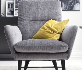 Sessel mit grauem Stoffbezug und gelben Deko-Kissen neben einem eleganten Beistelltisch