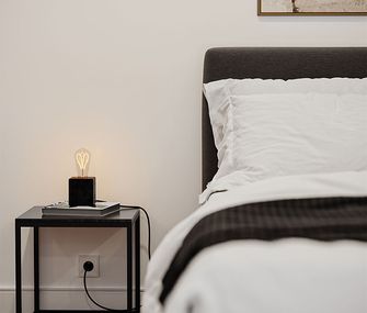 Nahaufnahme des Bettes und Beistelltisches in Schwarz mit einer Tischleuchte aus einer Glühbirne
