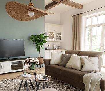 Wohnzimmer im Landhaus-Look mit braunem Sofa, Beistelltischen, beigem Hocker auf hellgrauem Teppich.