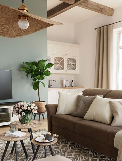 Wohnzimmer im Landhaus-Look mit braunem Sofa, Beistelltischen, beigem Hocker auf hellgrauem Teppich.