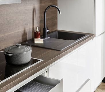 Weiße Küche mit Arbeitsplatte in dunklem Holz, schwarzem Spülbecken und Kochfeld von Neff.