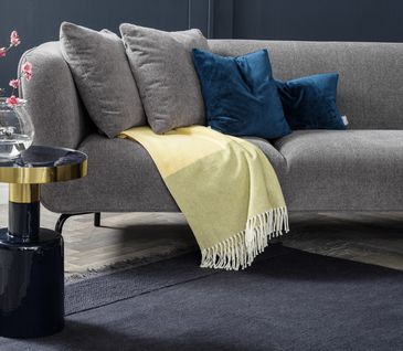 Dunkelgraues Stoff-Sofa mit blauen Kissen und einer gelben Wohndecke