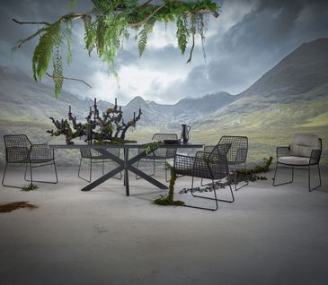 Großer, moderner Gartentisch mit sechs Gartenstühlen, gepolstert und geflochten.