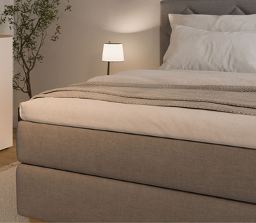 Detailbild der Ecke eines warmgrauen Boxspringbettes in harmonischem Ambiente