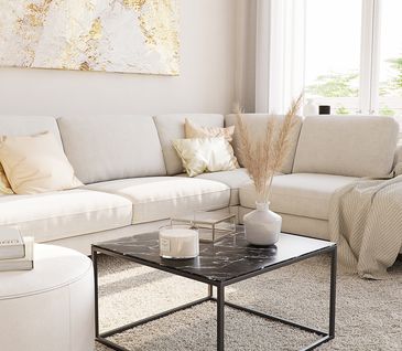 Sofa in Cremeweiß vor einem schwarzen Couchtisch mit Marmor-Optik