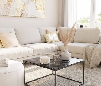 Nahaufnahme eines weißen Ecksofas hinter einem schwarzen eckigen Couchtisch mit einer Keramikplatte in Marmoroptik